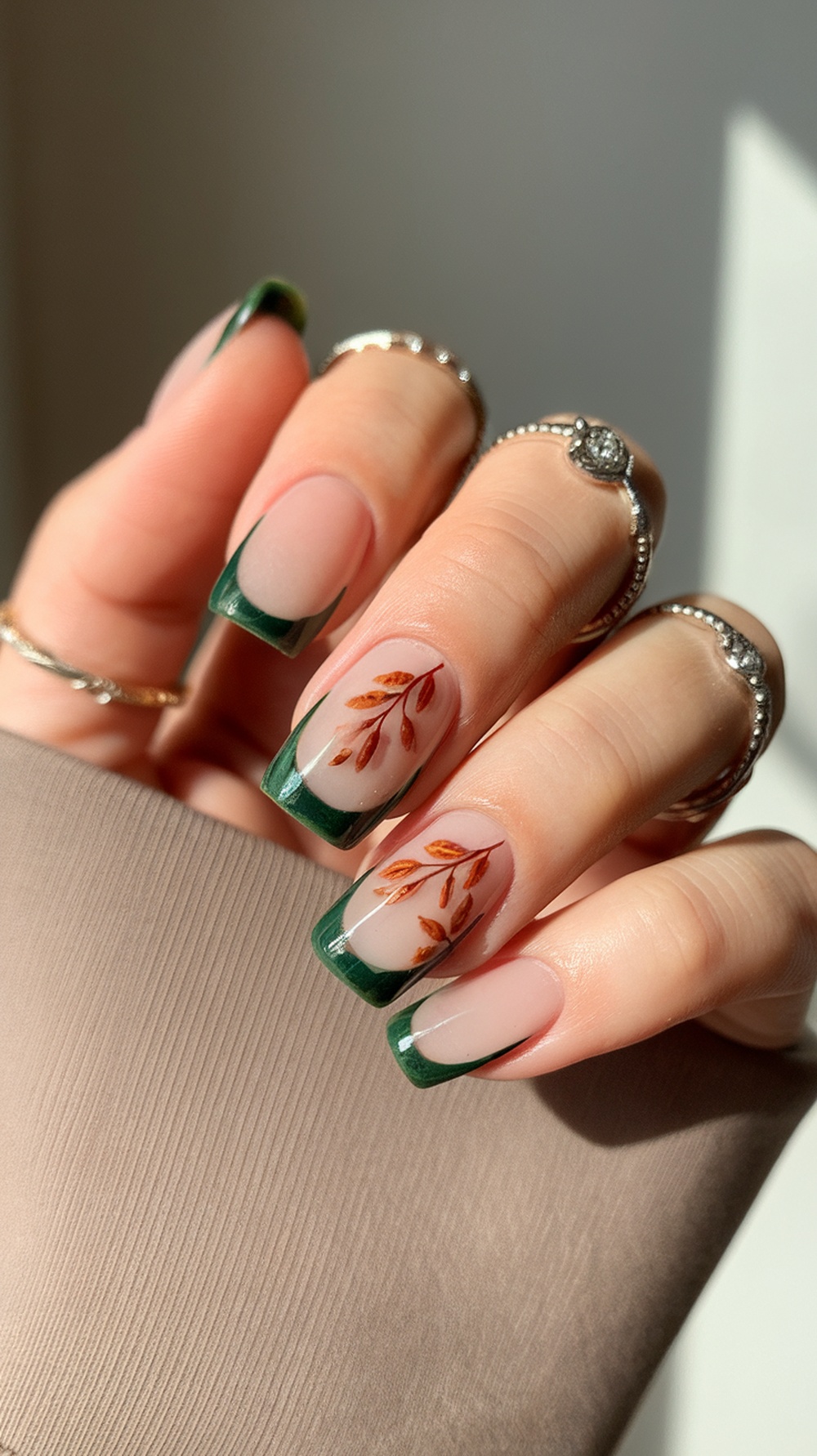 Nails featuring muted green tips on a neutral base with leaf designs.