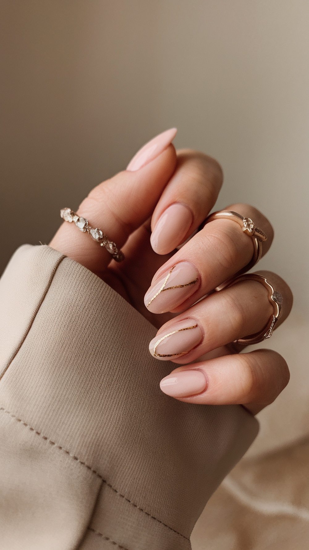 A hand with rounded nails painted in a soft color, adorned with rings, showcasing a stylish and elegant look.