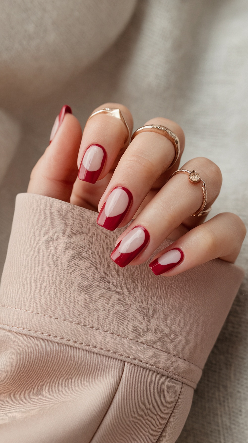 A hand with negative space red nail design, showcasing red tips and clear sections, adorned with rings.