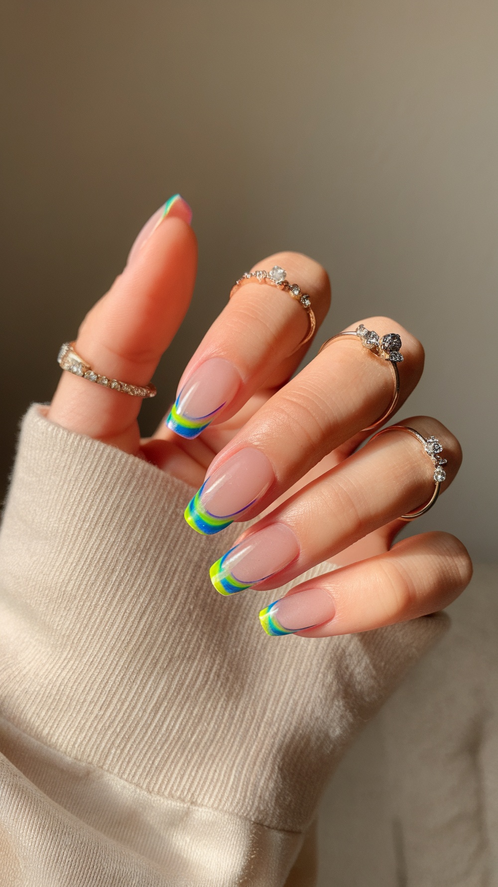 Close-up of hands with neon rainbow nail design featuring colorful tips and delicate rings.