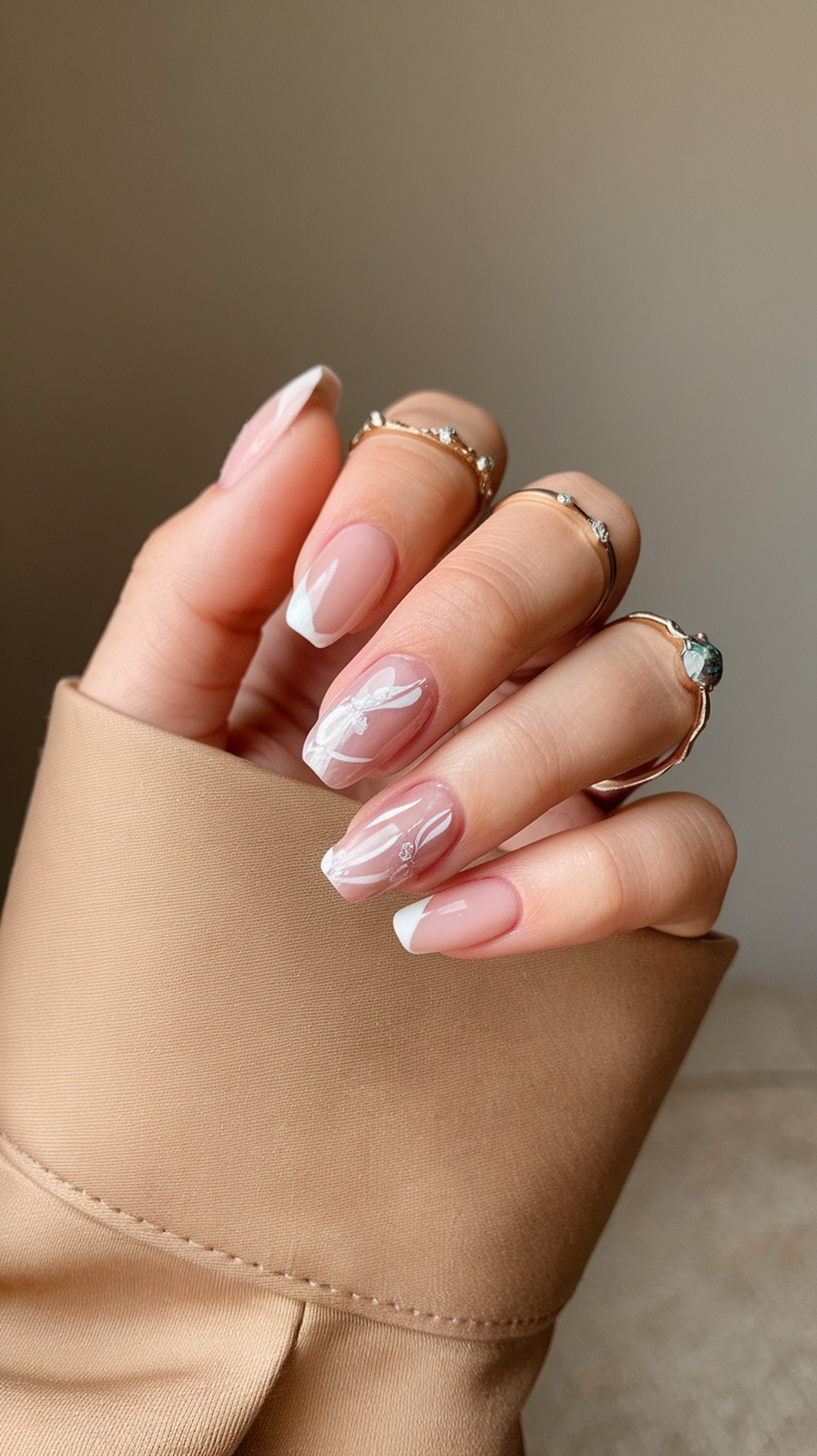 A hand with nude pink nails featuring floral nail art, adorned with rings, resting on a beige fabric.