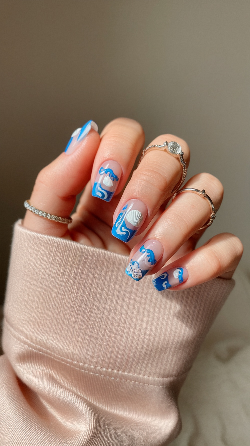 Ocean-inspired nail design featuring blue waves and white shells on a hand with rings