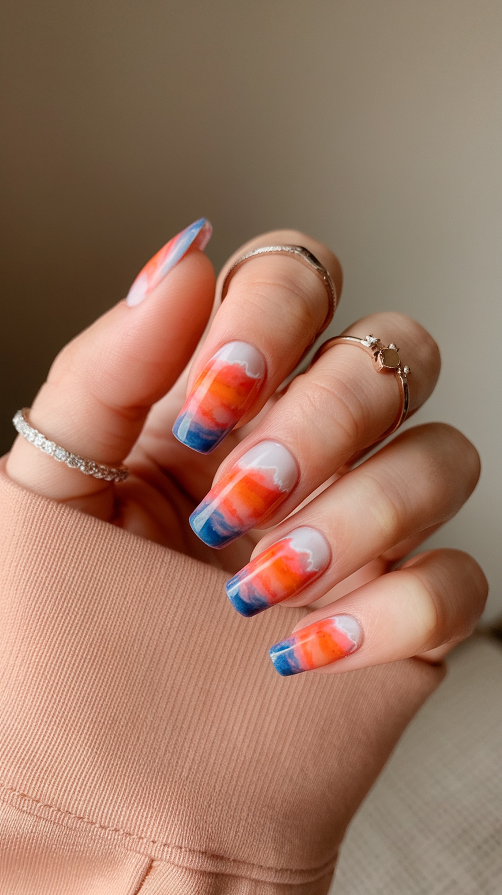 Nails with an ocean sunset gradient design featuring orange and blue colors.