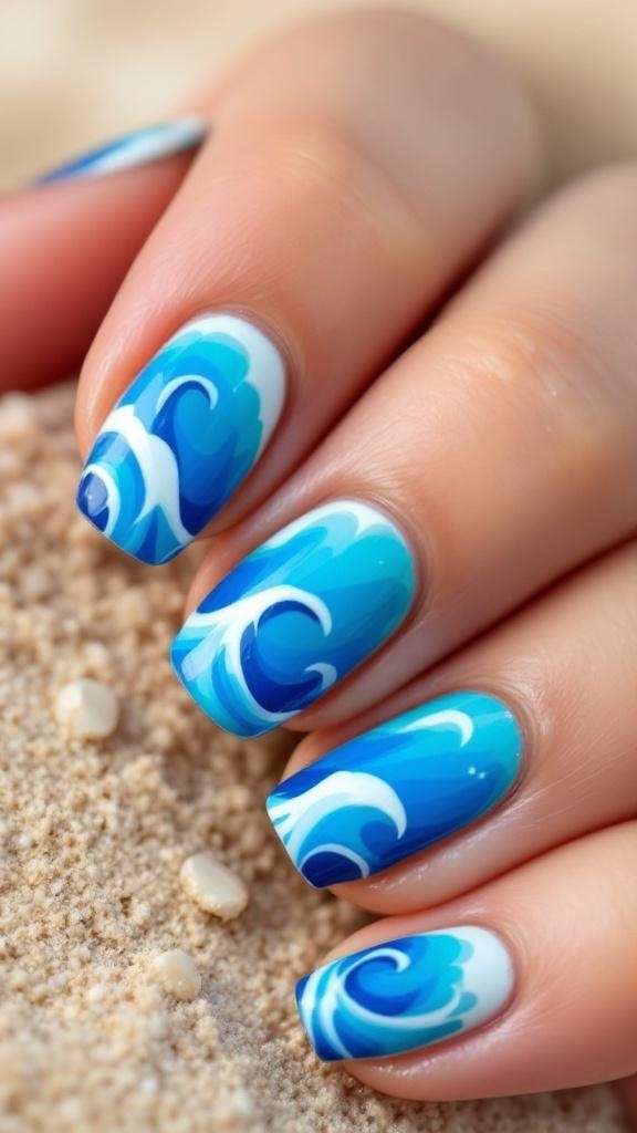 A hand with ocean wave nail art featuring blue and white designs on the nails, set against a sandy background.