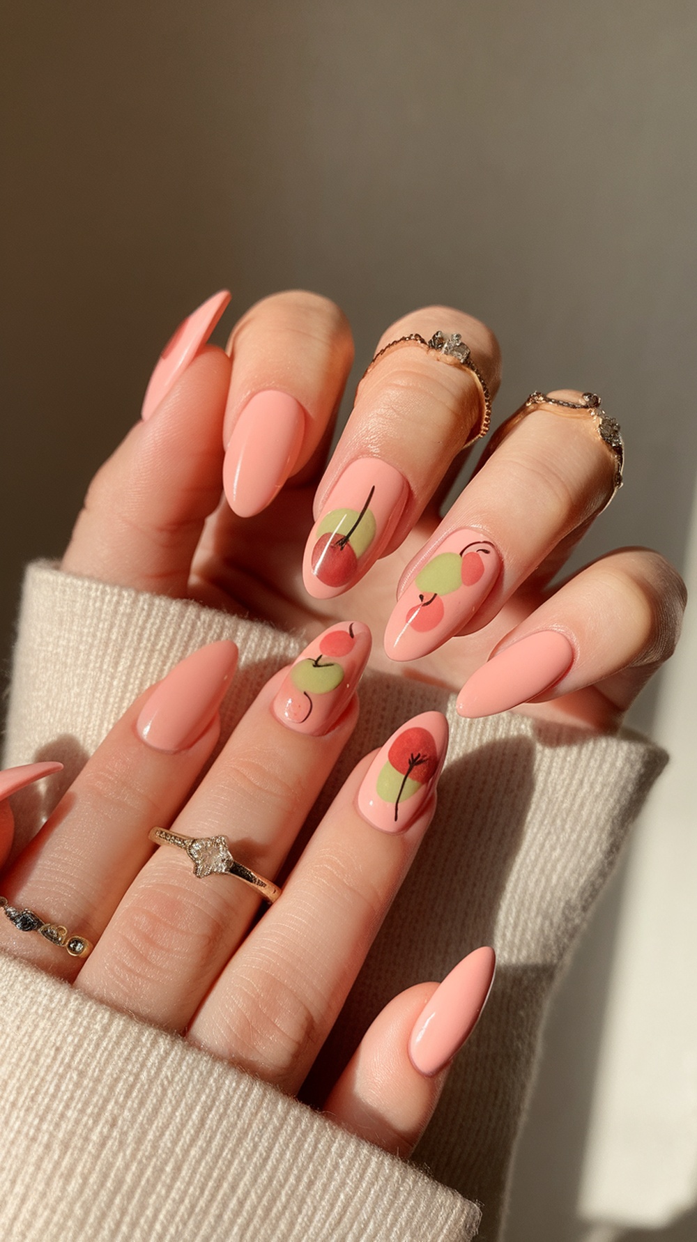 A hand with peachy pink almond nails featuring floral designs, showcasing a stylish and fresh fall nail art.