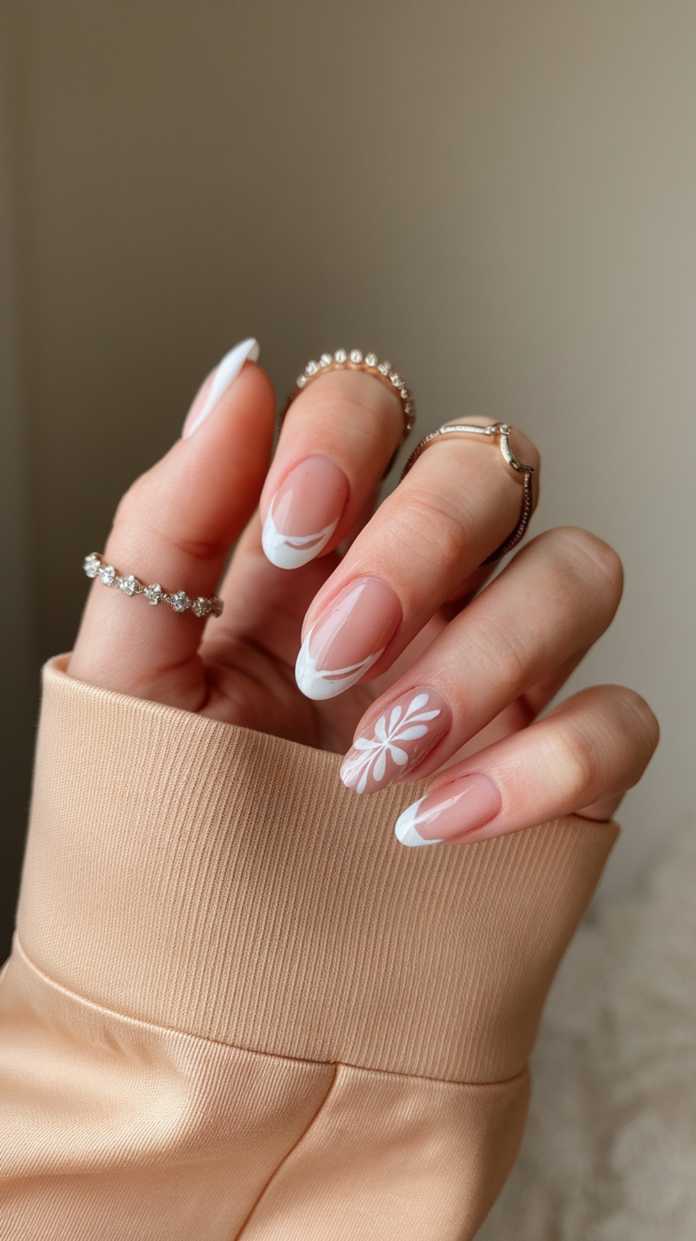 A hand with beautifully manicured nails featuring a soft base and white accents, showcasing a modern nail design.