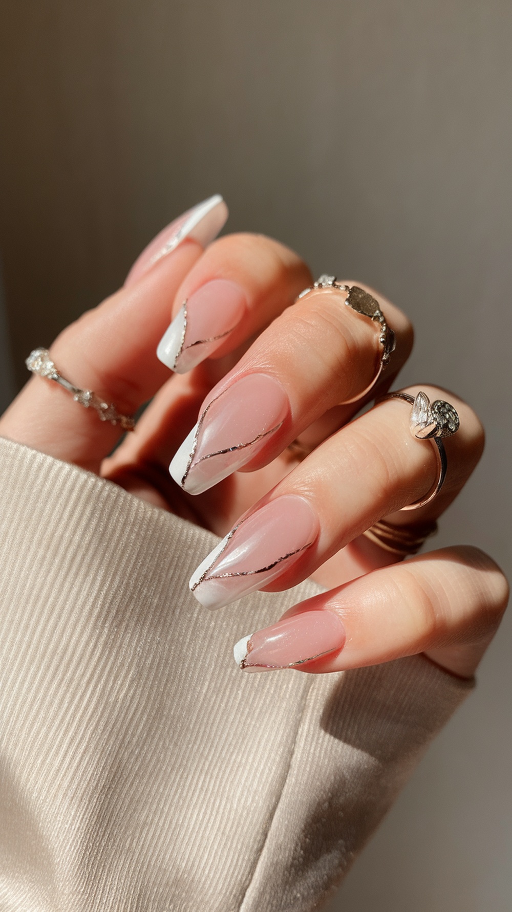 A close-up of slim nails with a pink and white design, featuring gold accents, showcasing a professional manicure.