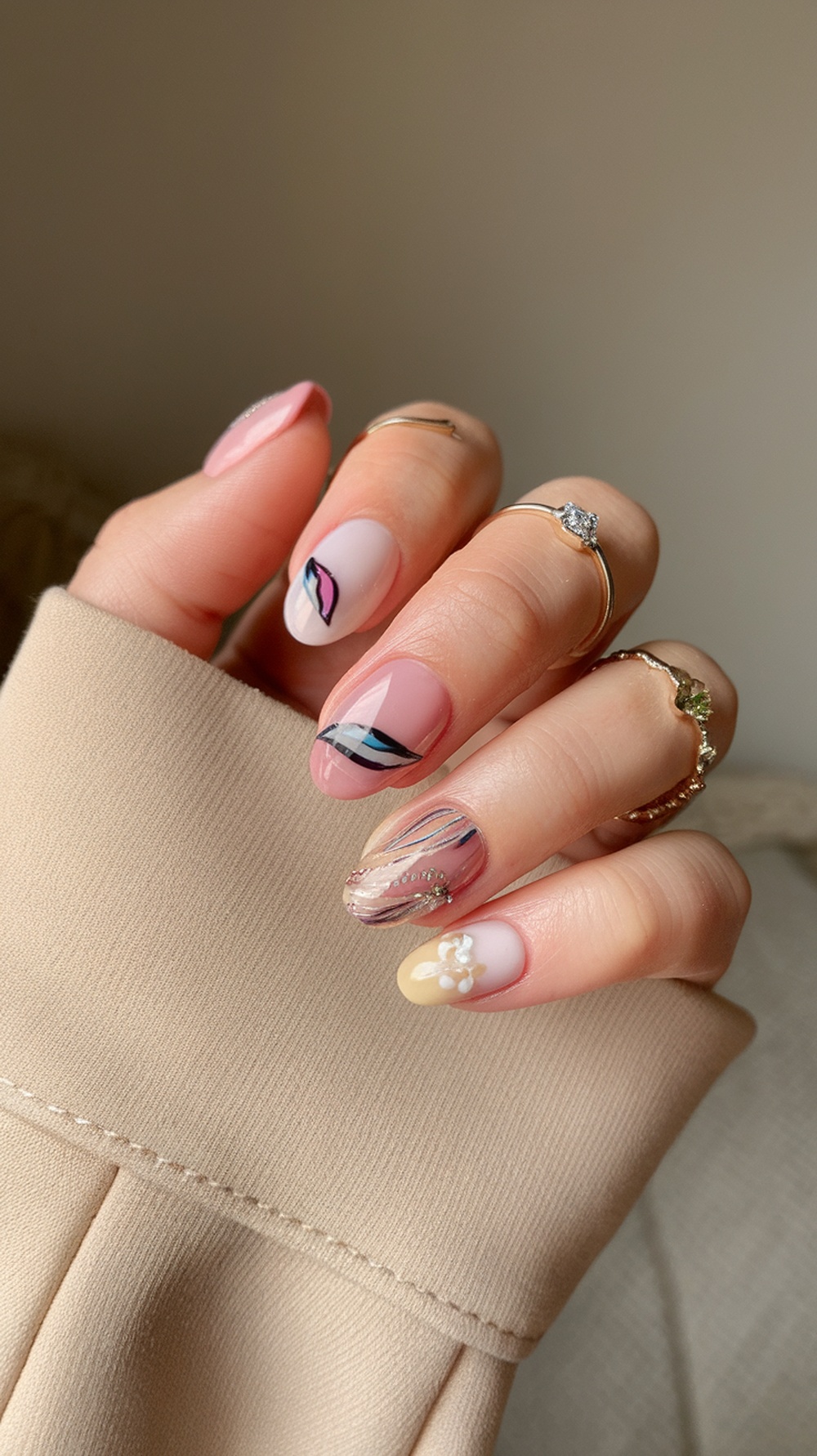 A close-up of a hand with rounded nails featuring various designs, including floral and geometric patterns, set against a soft background.