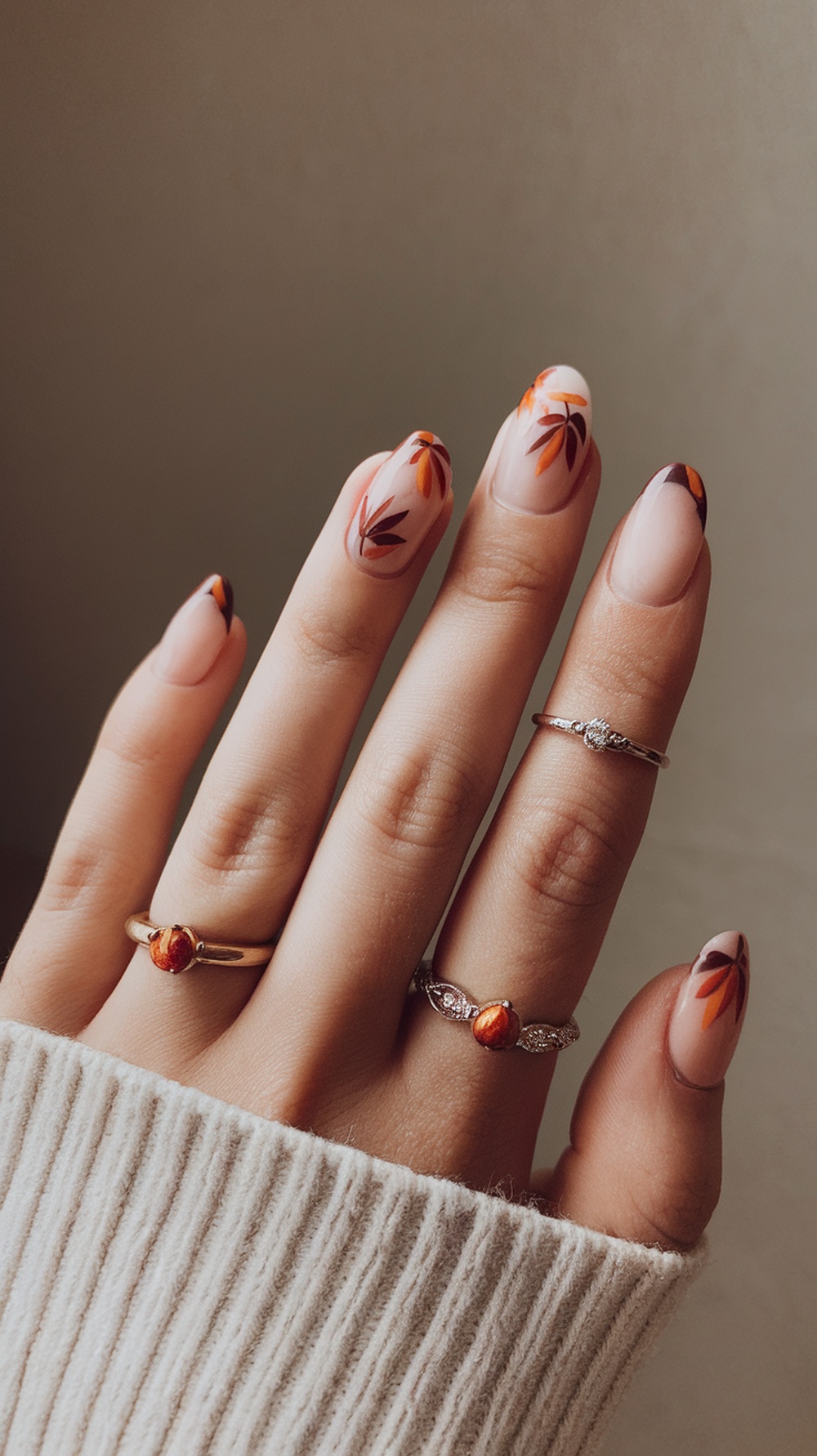 A hand with seasonal French nails featuring floral designs in warm colors, adorned with rings.