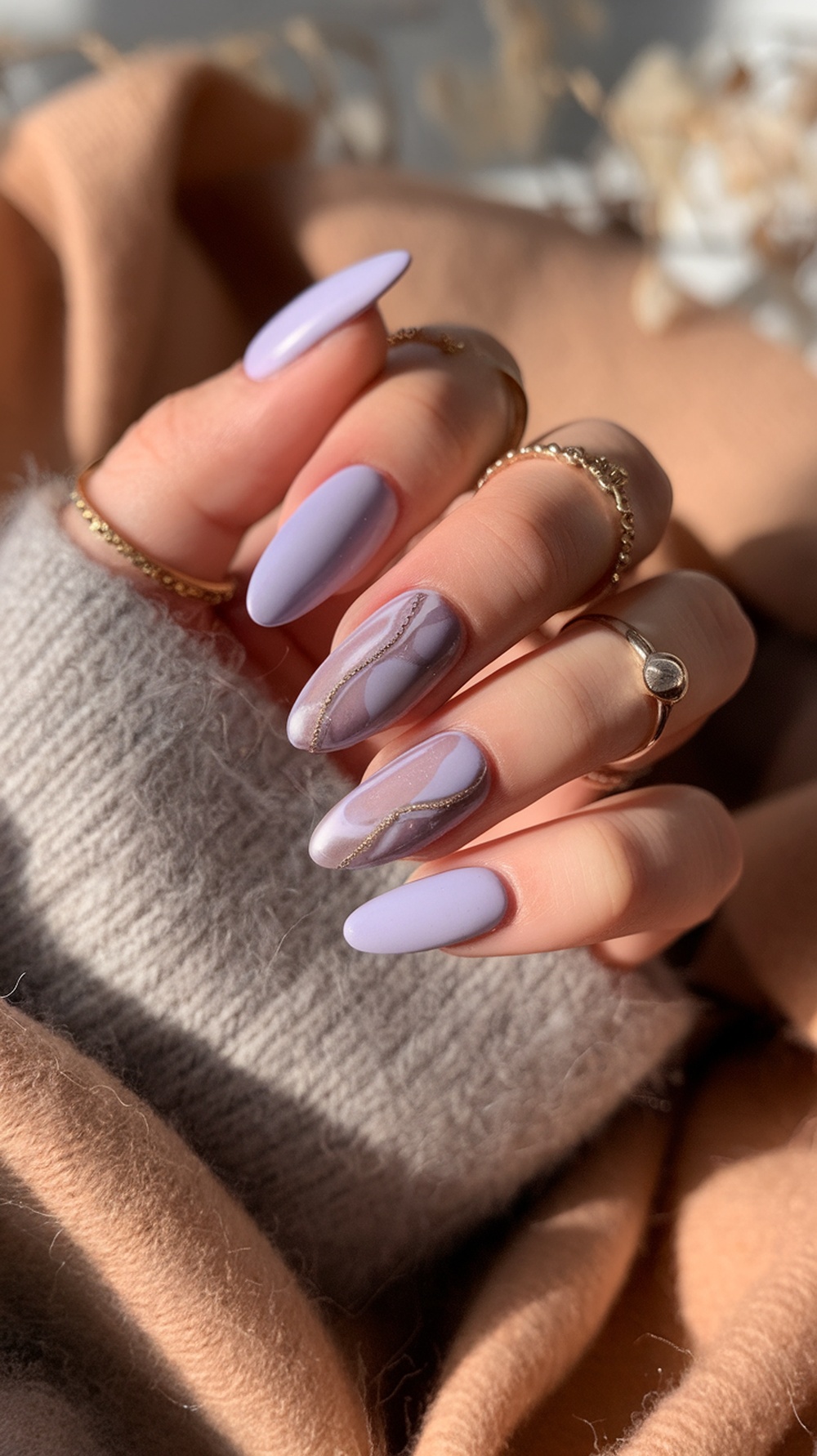 Soft lavender almond nails featuring elegant swirls and gold accents, set against a cozy sweater backdrop.