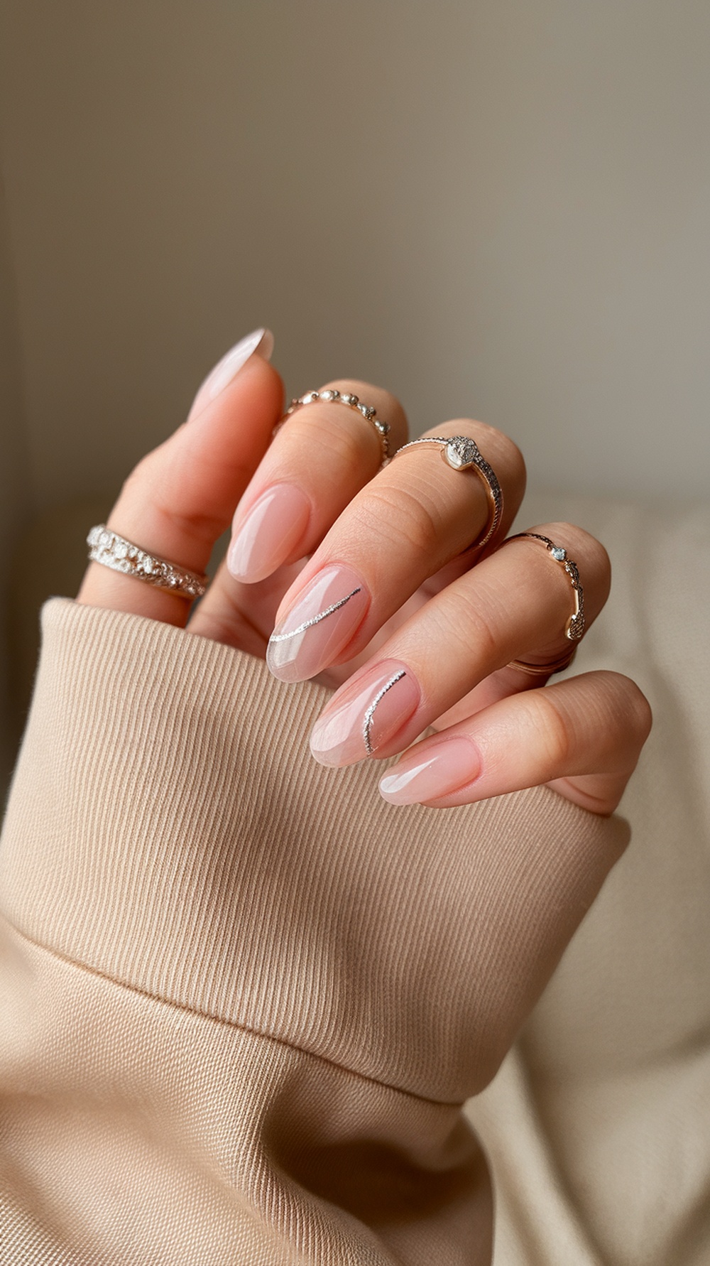 Close-up of soft pink nails with glitter tips, adorned with rings on fingers.