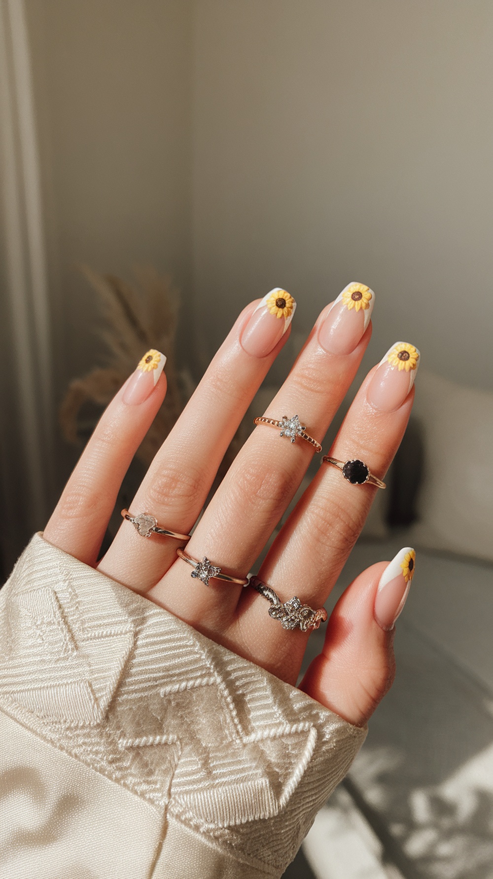 A hand with sunflower French manicure, featuring nude nails with sunflower tips and elegant rings.