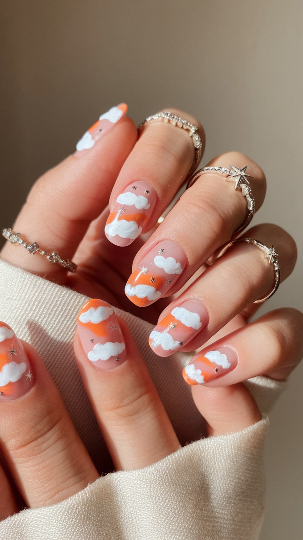 Nails painted with sunset colors, clouds, and stars