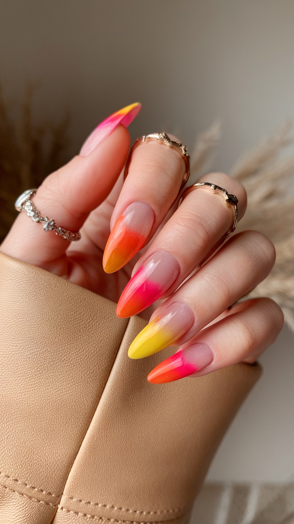 A hand displaying sunset gradient almond nails with pink, orange, and yellow colors.
