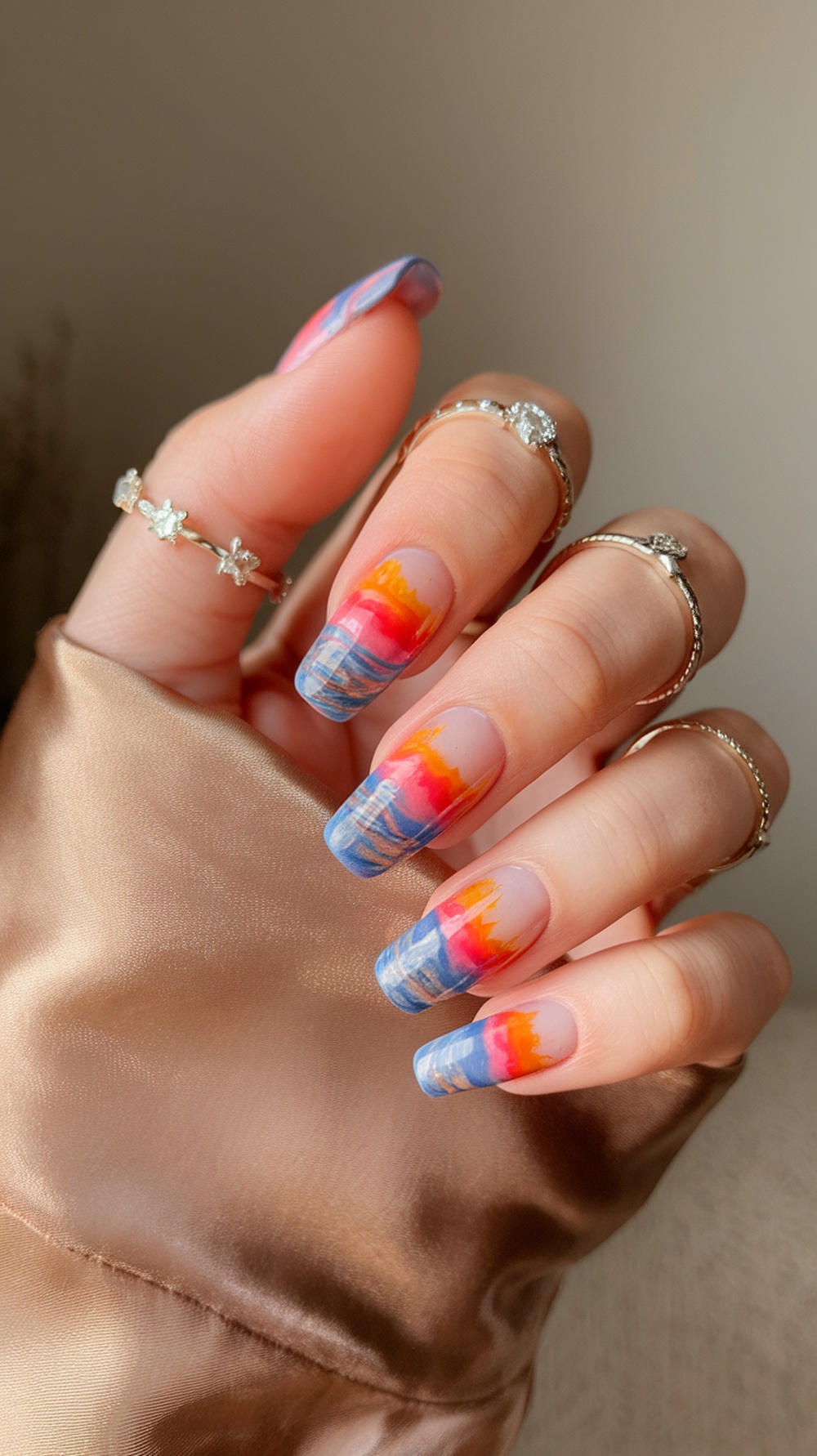 Nail design featuring sunset colors reflecting on water with rings on fingers