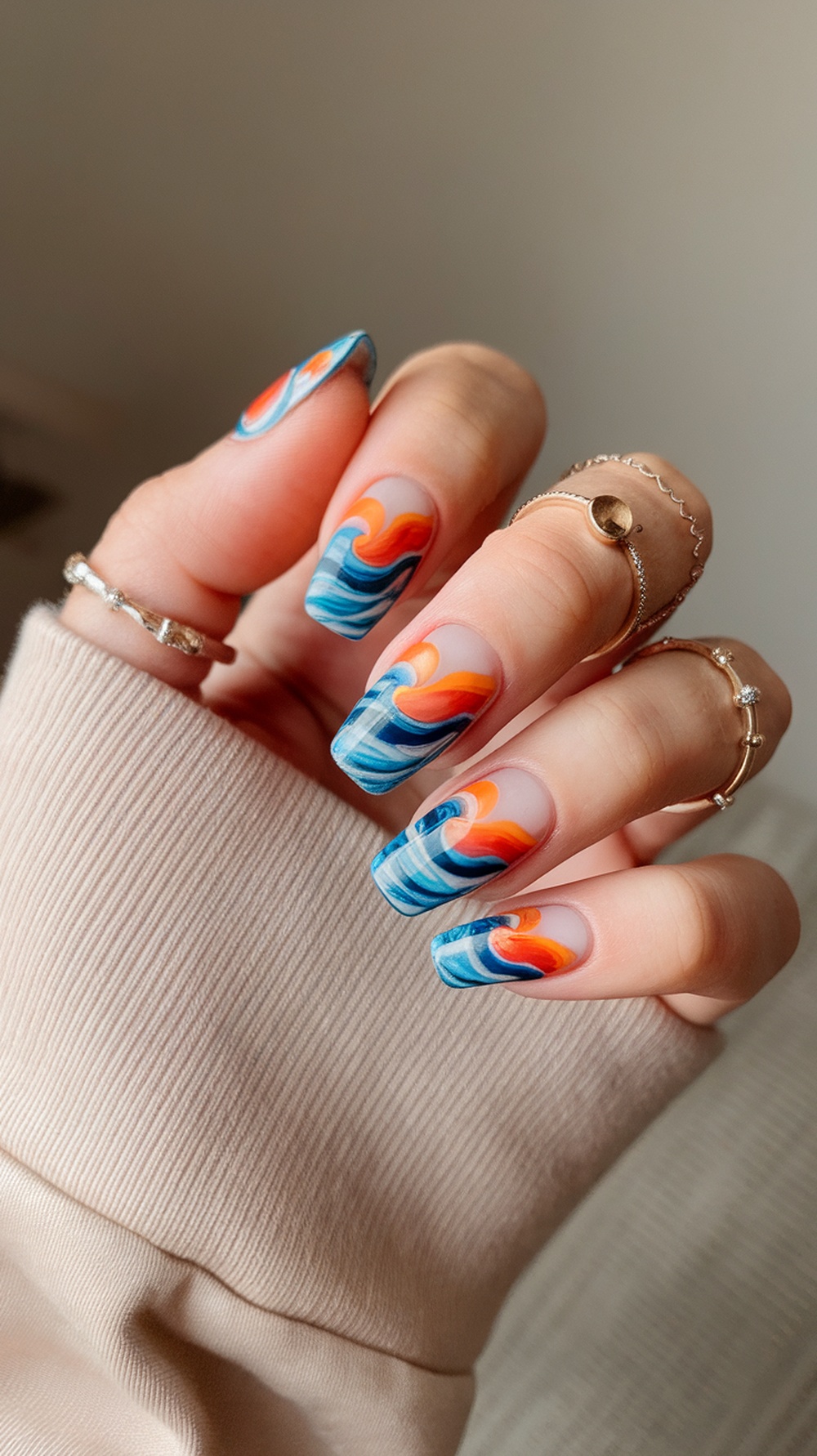 Nails painted with sunset waves design featuring vibrant orange and blue colors.
