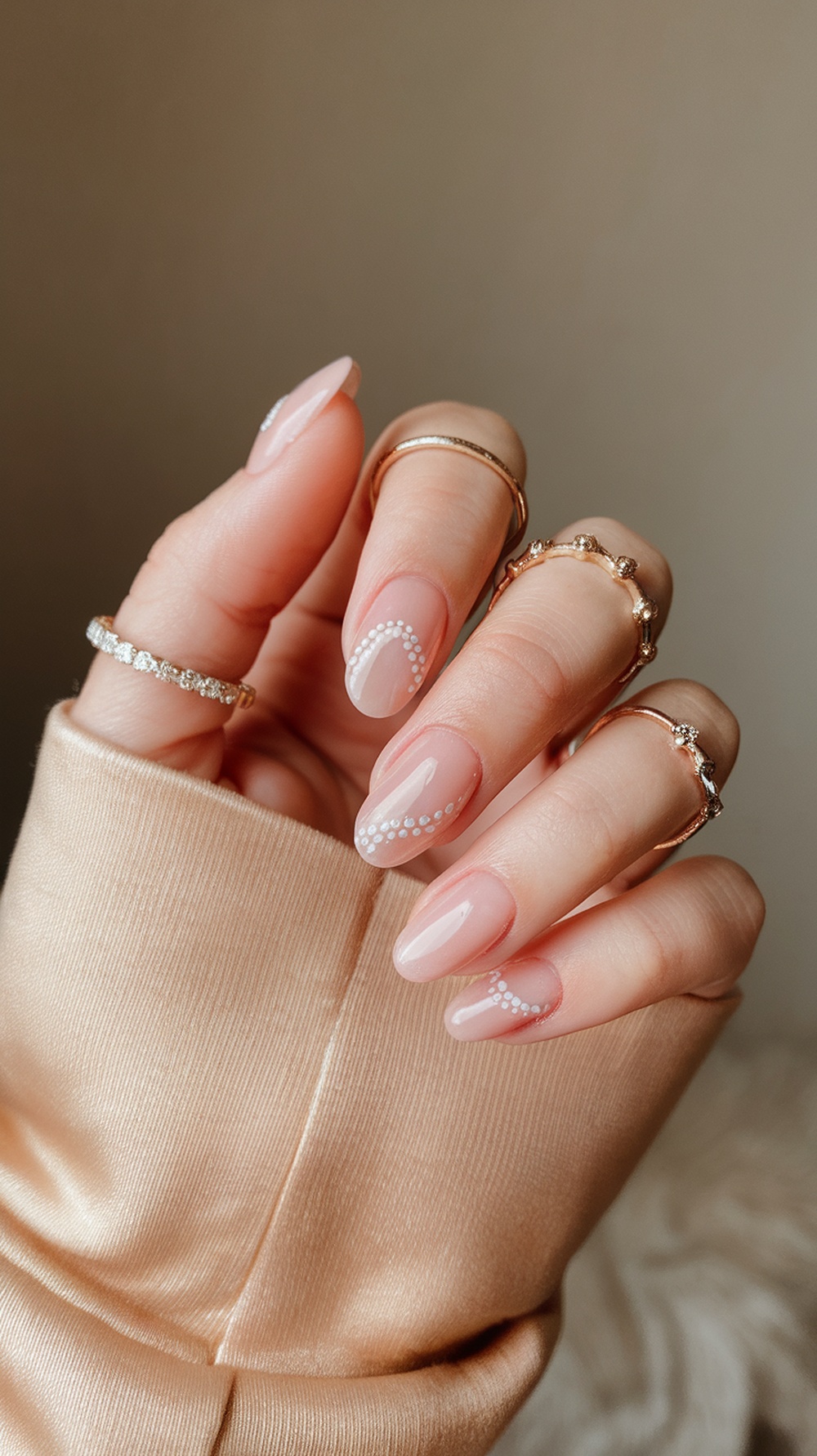 A close-up of hands with pink nails featuring rhinestone designs, wearing multiple rings.
