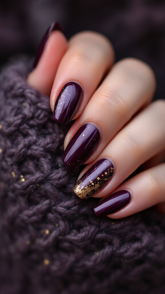 Nails painted deep plum with gold foil accents on a knitted background.