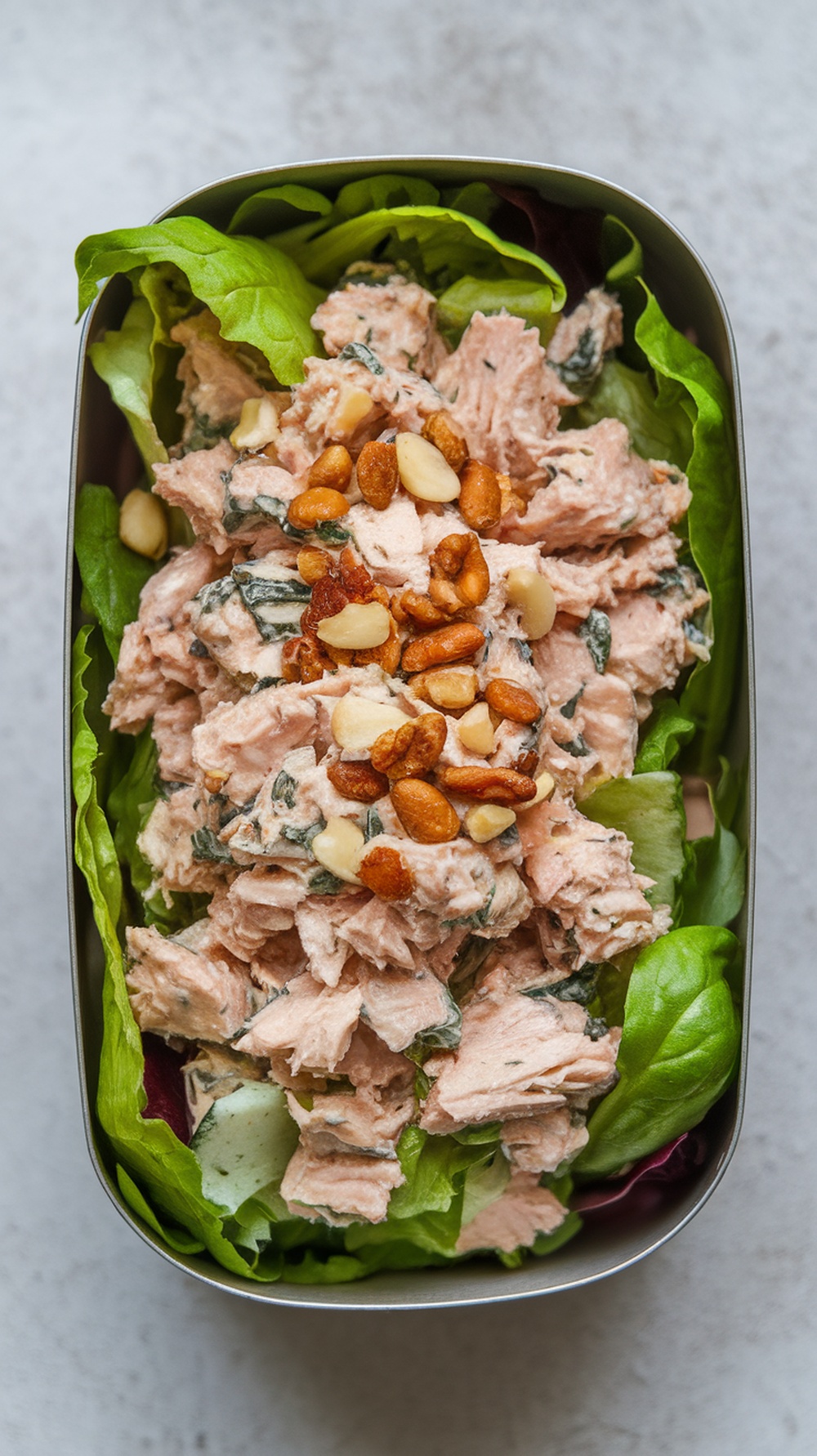Tuna salad served on mixed greens, topped with nuts in a lunch container
