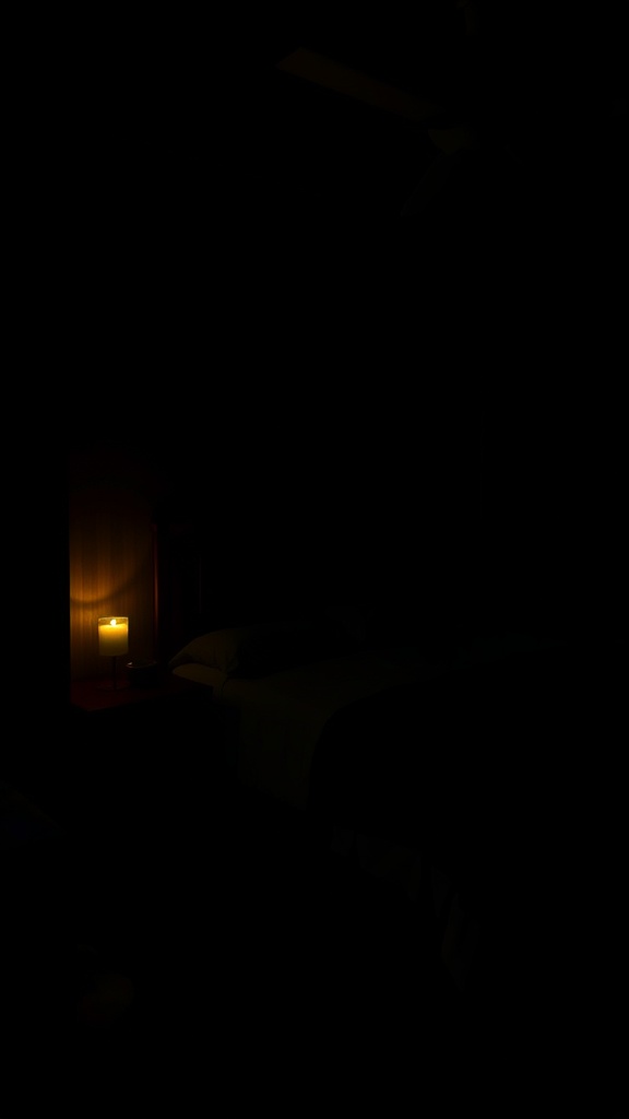 A dark bedroom with a glowing candle on a bedside table