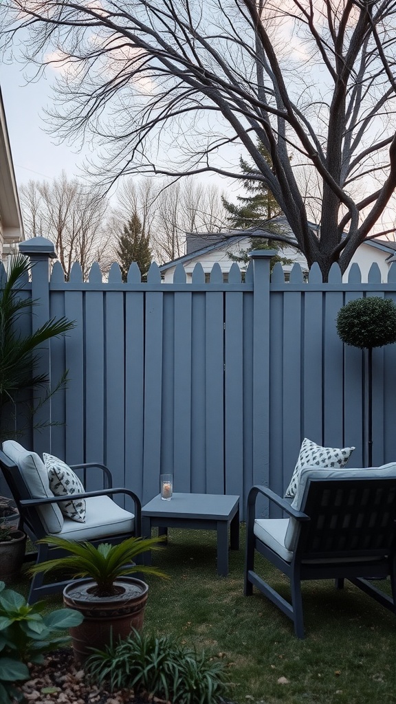 A cozy outdoor seating area featuring a calming gray fence, with two chairs, a small table, and various plants.