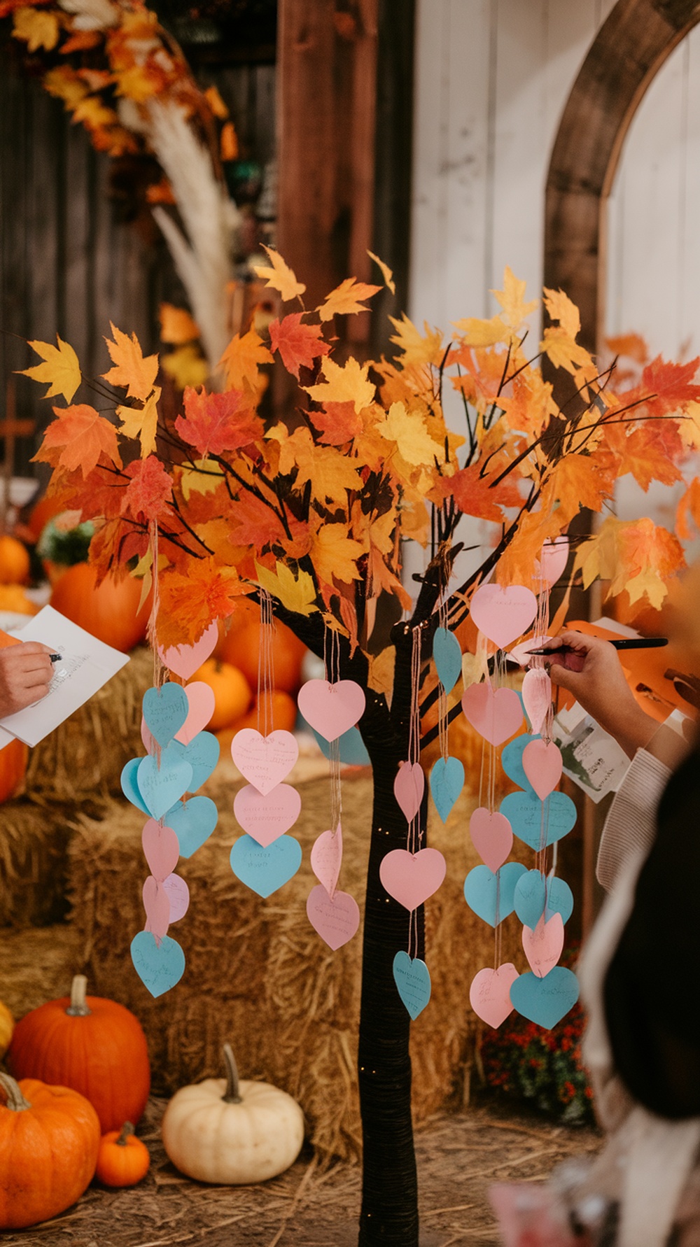A decorative tree with colorful leaves and heart-shaped cards hanging from it, surrounded by pumpkins.