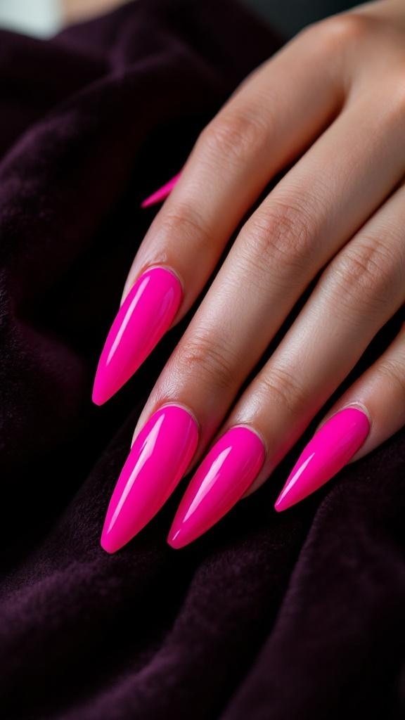 Bright fuchsia stiletto nails on a hand resting on a dark fabric background.