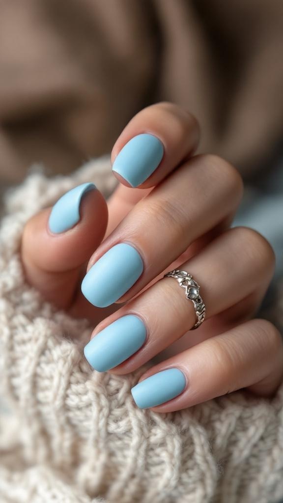 Close-up of hands with sky blue matte nails and a silver ring, resting on a knitted sweater.