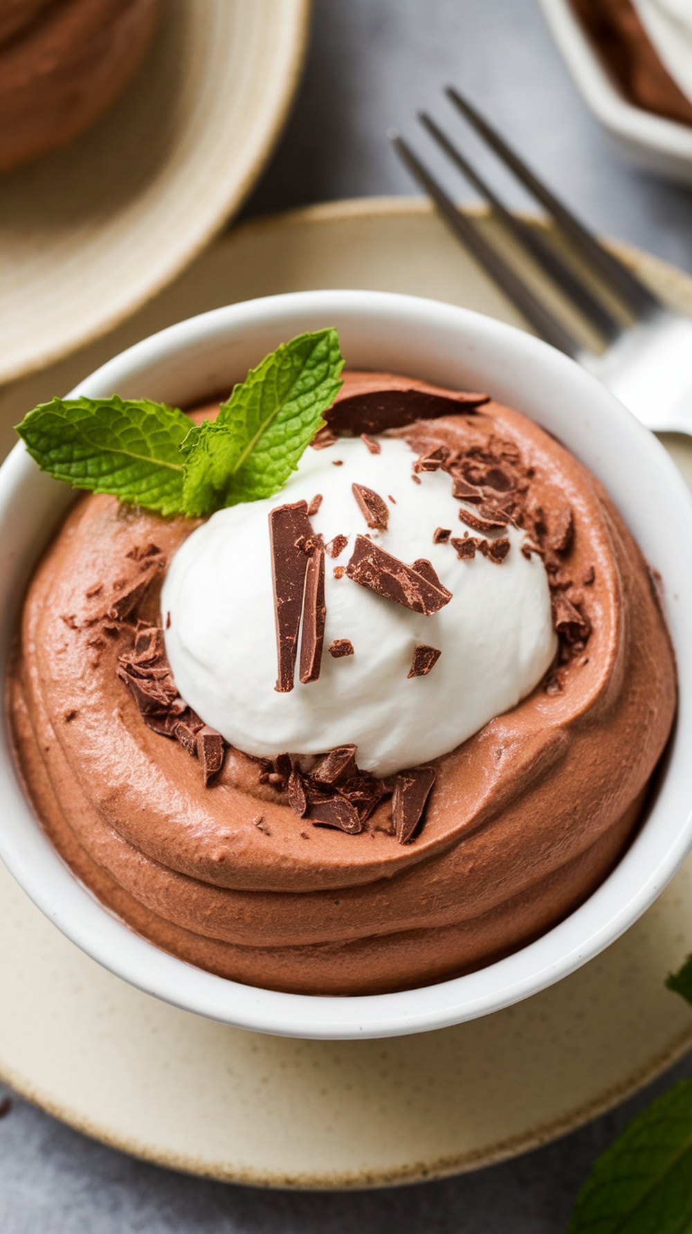 A creamy bowl of cottage cheese chocolate mousse topped with whipped cream and chocolate shavings, garnished with a mint leaf.