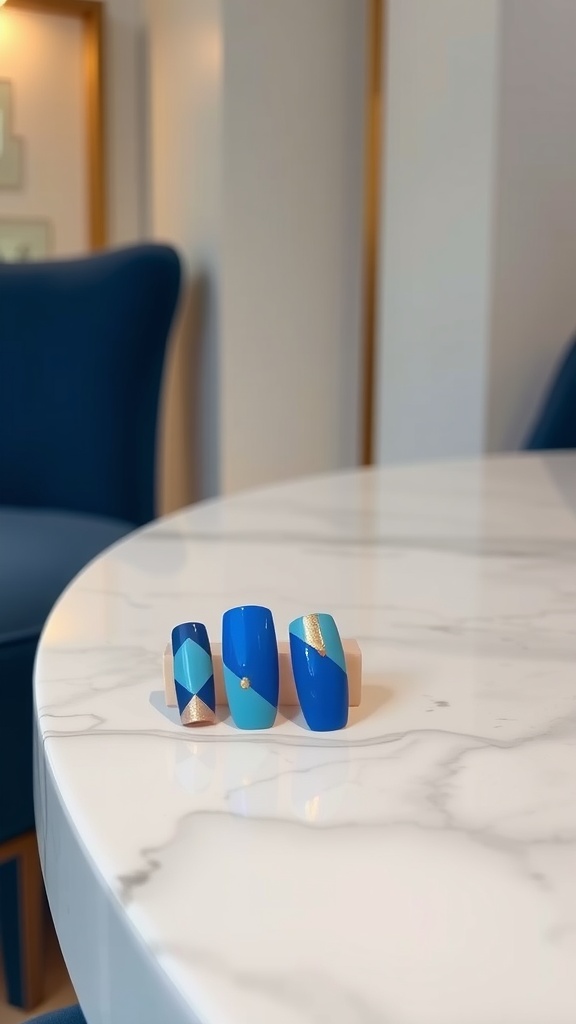 Three geometric blue nail designs displayed on a marble table.
