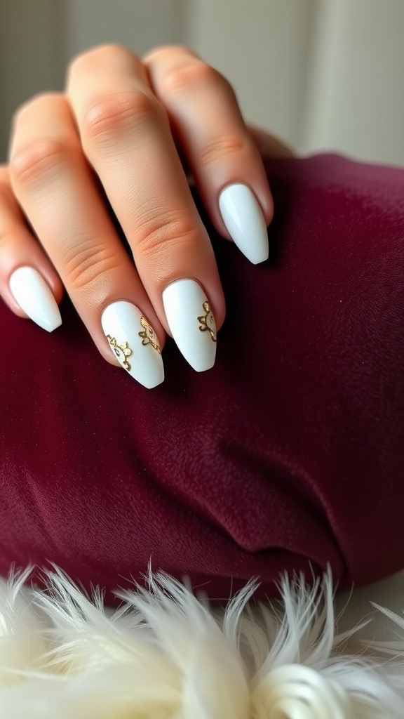 A hand with white almond nails adorned with gold foil accents resting on a burgundy fabric.