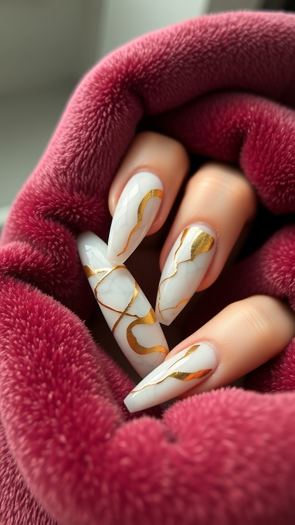 A close-up of nails featuring a marble effect with gold foil accents, resting on a plush burgundy fabric.