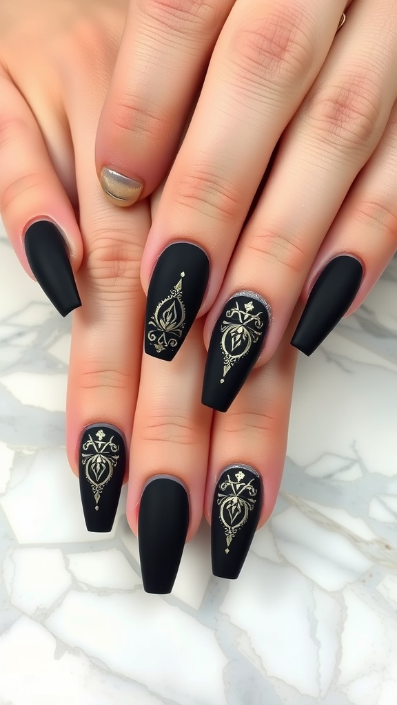 Matte black coffin nails featuring intricate gold accents and designs.