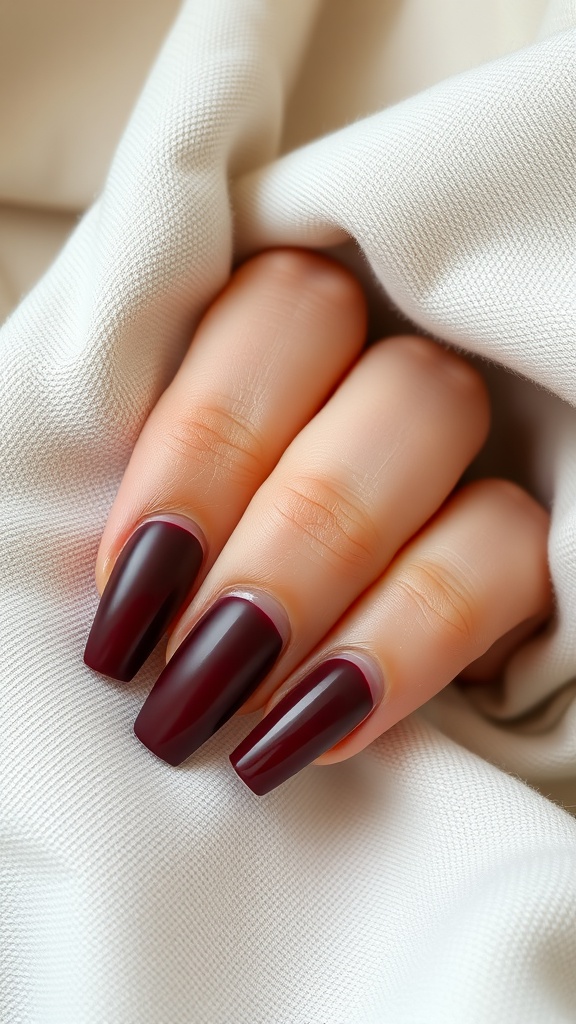 Close-up of a hand with matte finish coffin nails in deep burgundy color, resting on a light fabric.