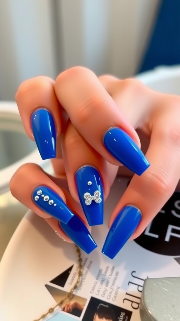 Close-up of royal blue acrylic nails with metallic studs and a bow design.