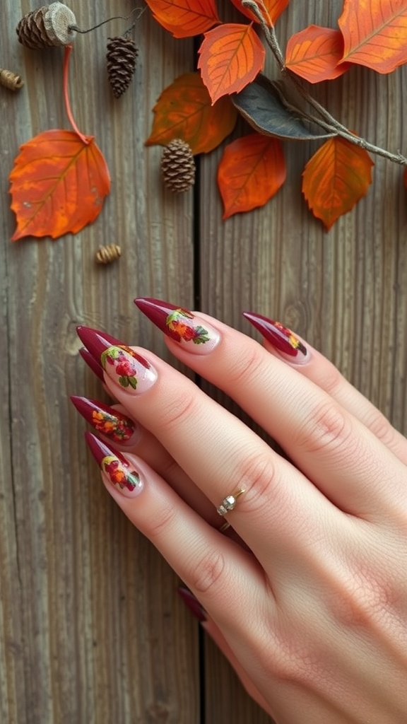Stiletto nails in burgundy with floral designs, surrounded by autumn leaves and pine cones.
