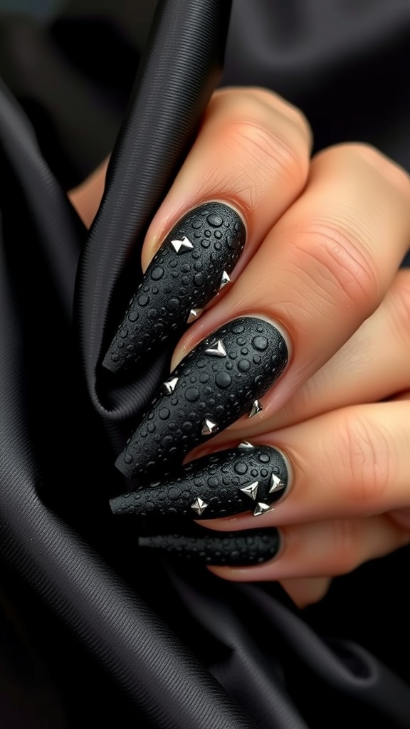Close-up of black coffin-shaped nails with textured surface and metallic studs.