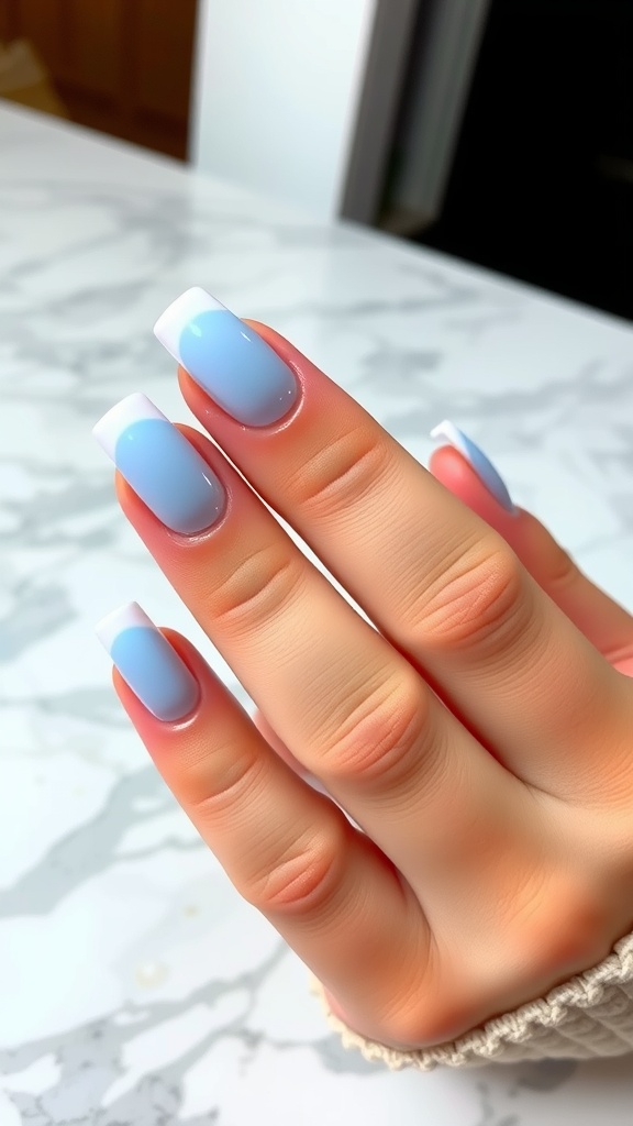 Close-up of hands with baby blue ombré acrylic nails on a marble surface.