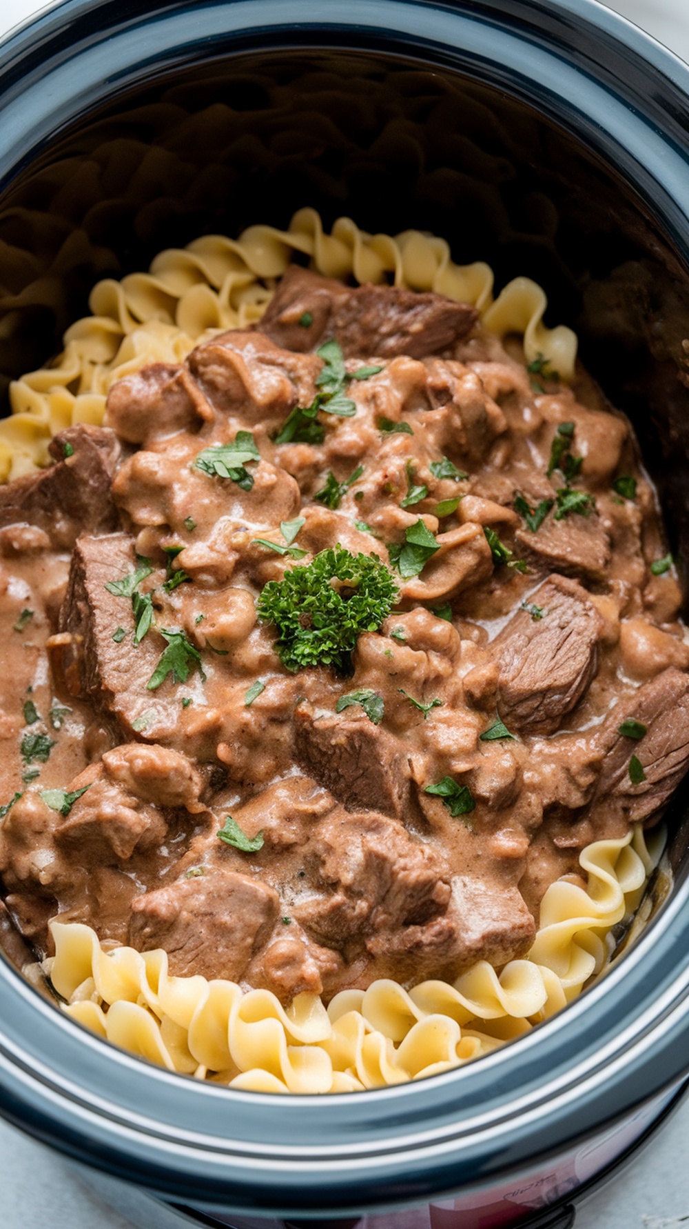 Crockpot Beef Stroganoff served over egg noodles, topped with fresh parsley.