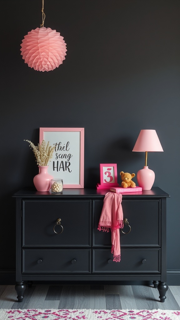 A black dresser with pink accessories, including a lamp, vases, and a framed print, set against a dark wall.