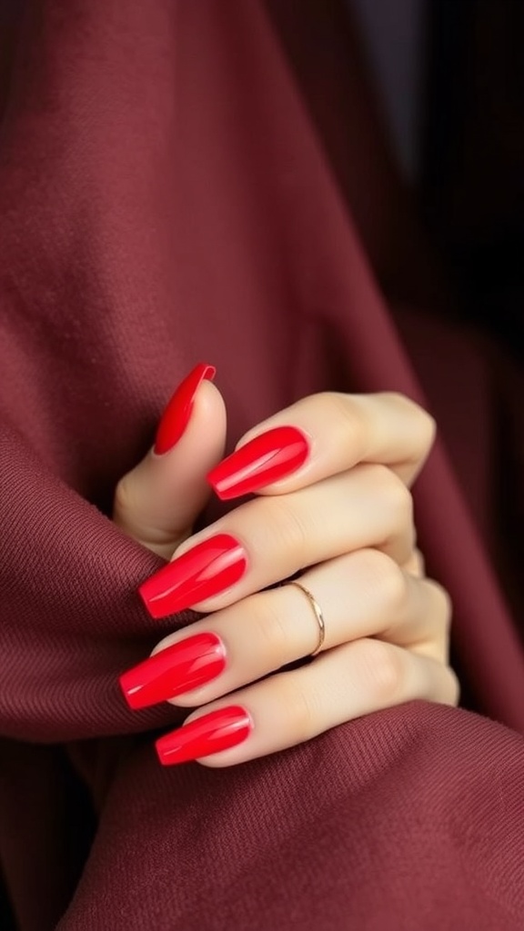 A close-up of elegantly manicured red acrylic nails resting on a burgundy fabric.