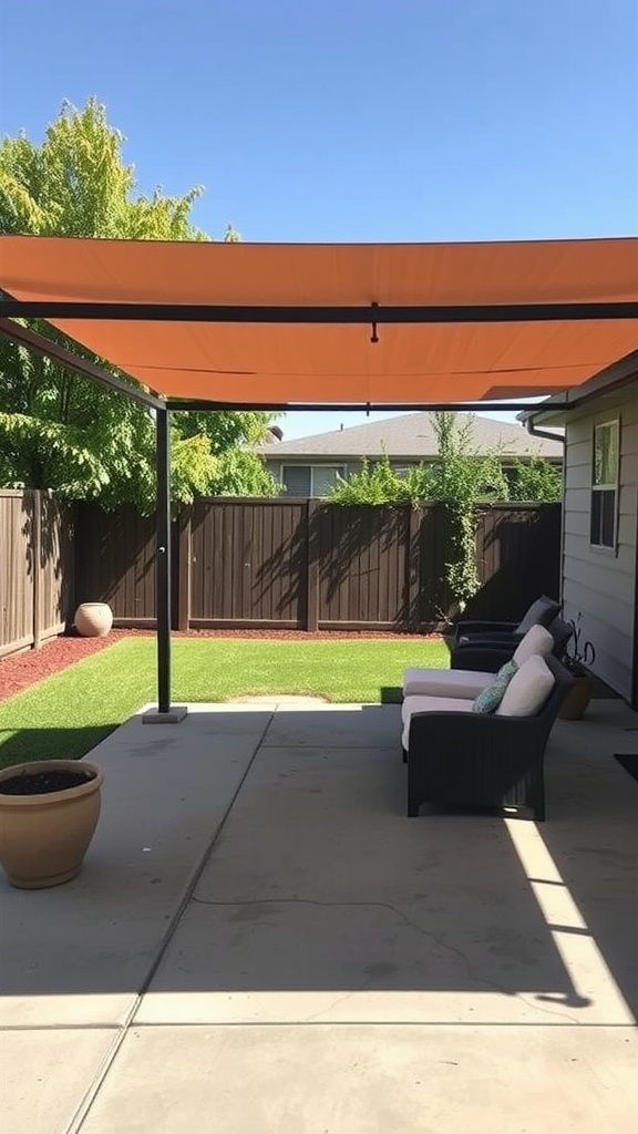 A cozy back patio with a concrete floor, shaded by an orange sail, featuring comfortable seating and green grass.