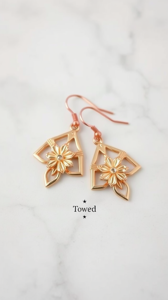 A pair of delicate rose gold earrings with floral design on a marble background.