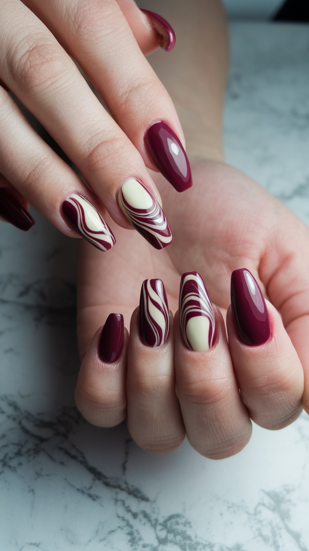 Nails featuring burgundy and cream swirl designs.