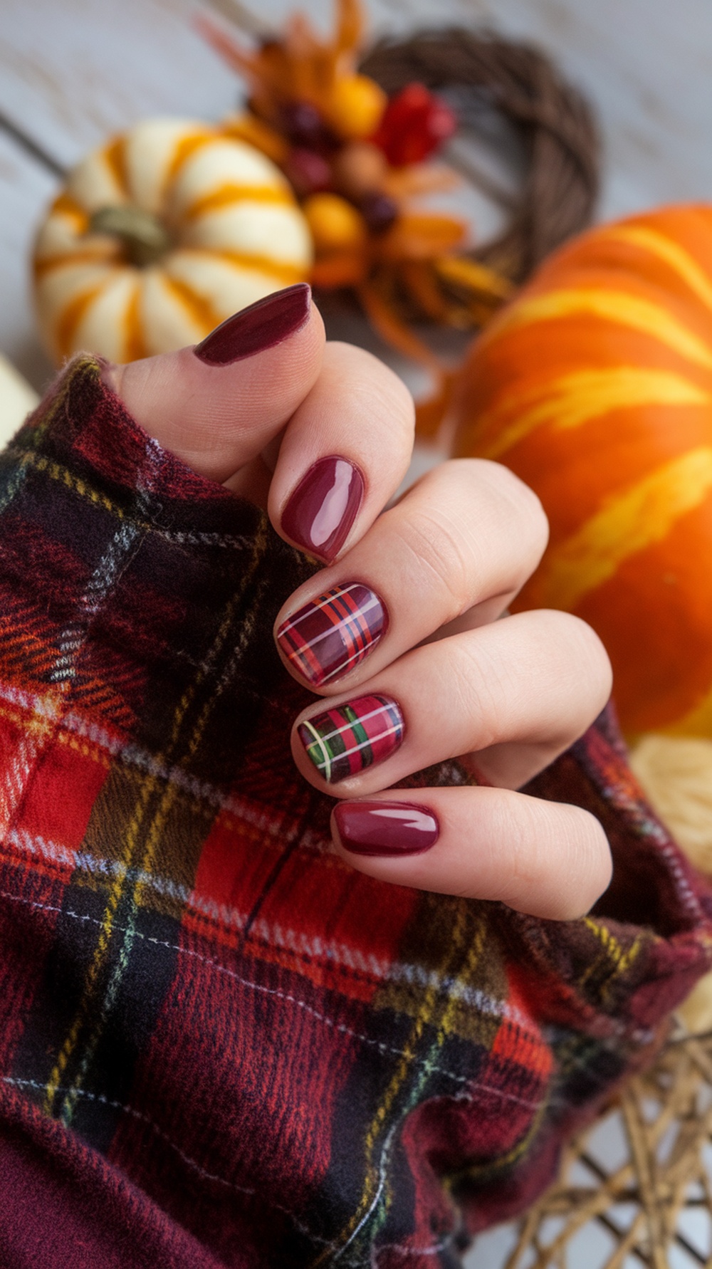 Burgundy nails with plaid design, autumn-themed decor in the background