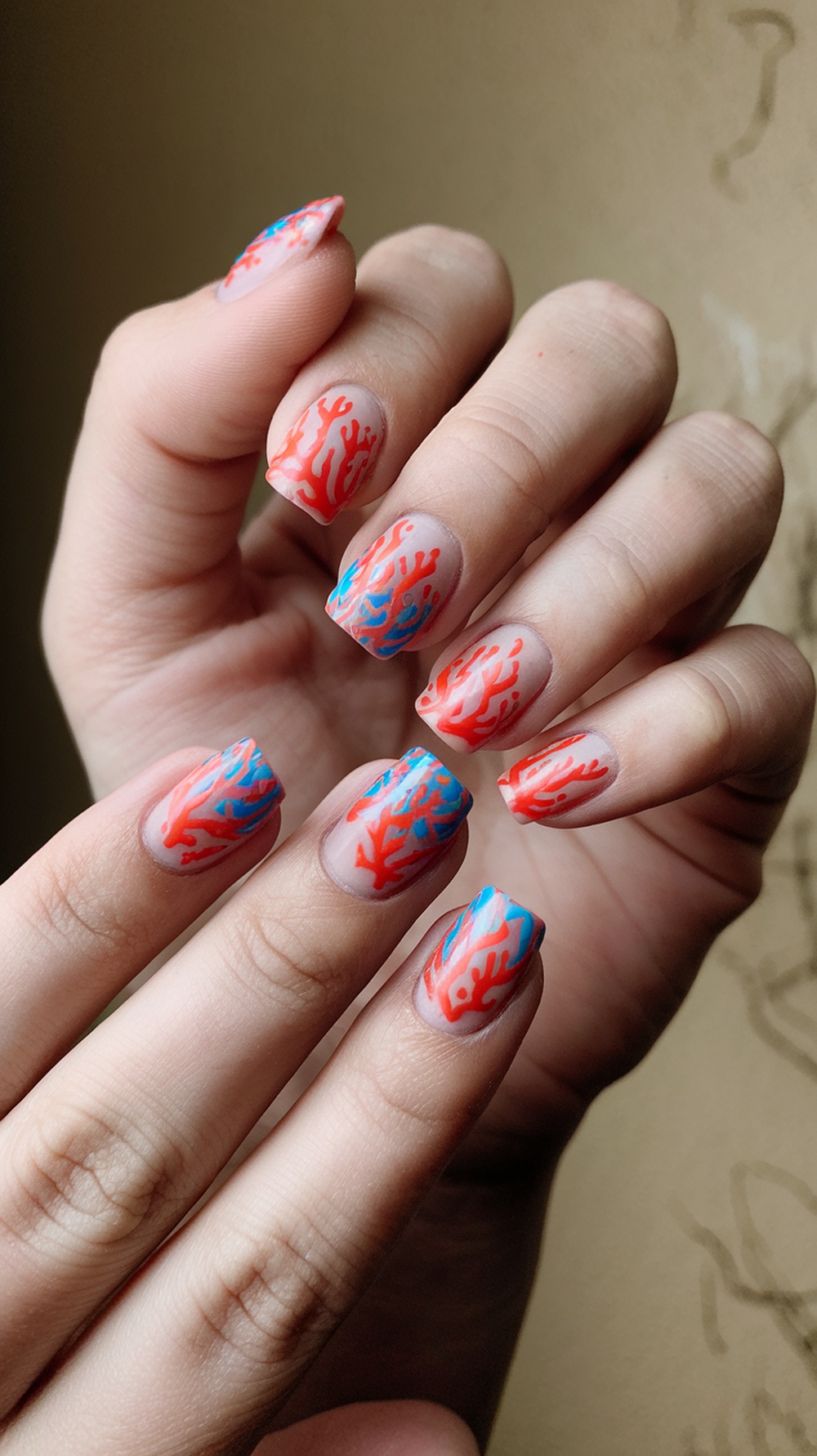 Nails featuring coral reef inspired designs with red and blue patterns on a clear base.
