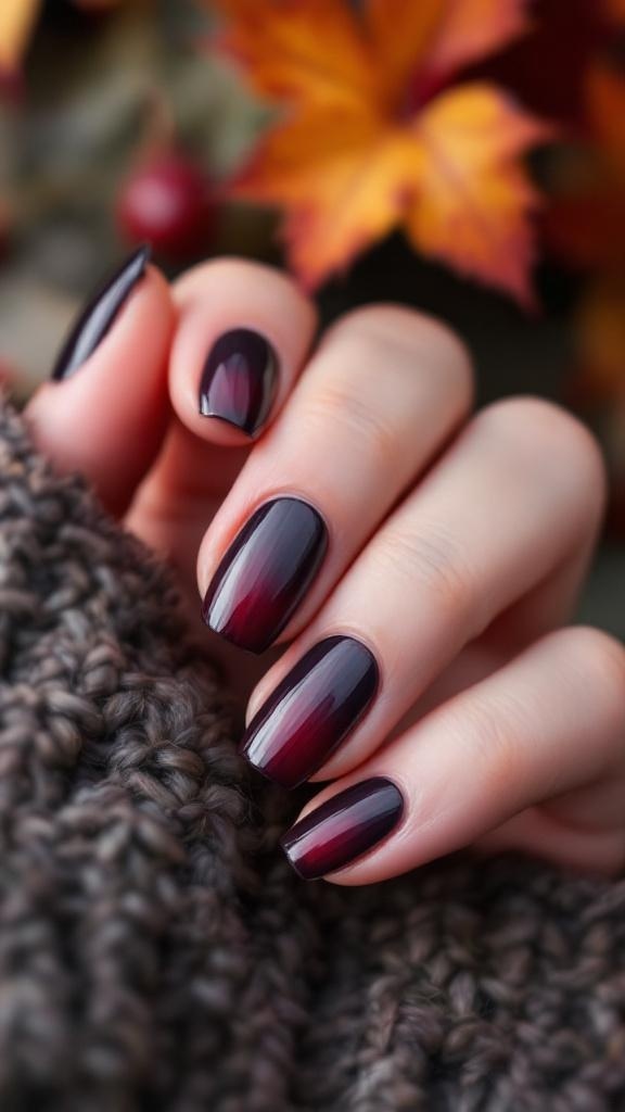 Dark cherry ombre nails with a glossy finish, set against a cozy knitted background and autumn leaves.