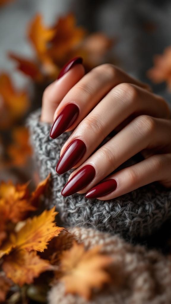 Dark cherry red nails with a matte finish, surrounded by autumn leaves and a cozy sweater.