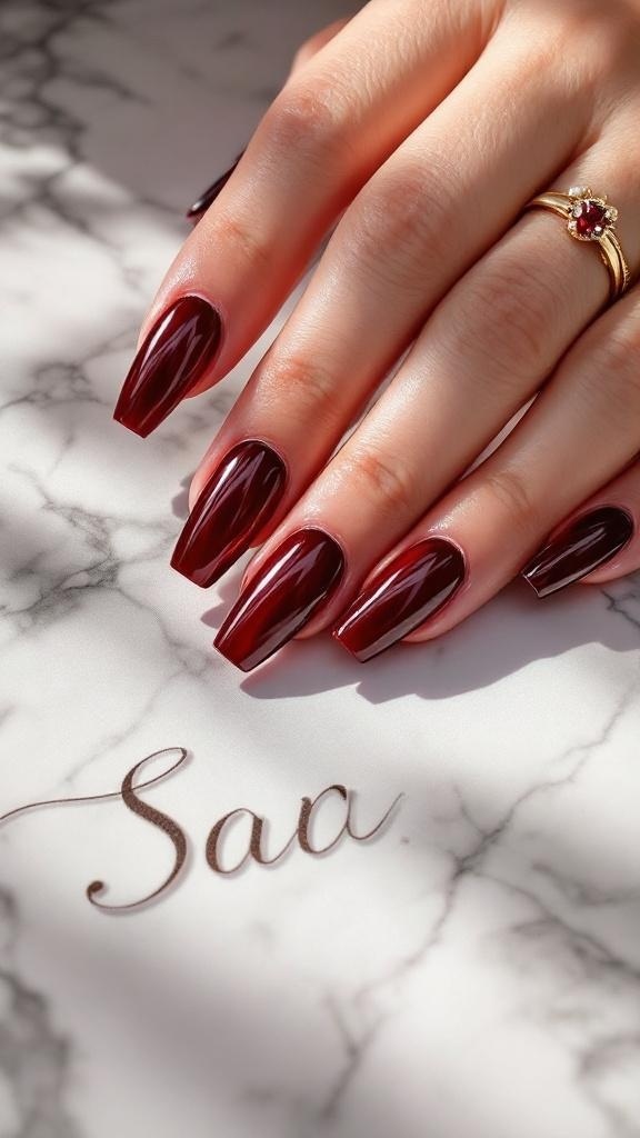 A hand with glossy cherry red nails resting on a marble surface, featuring a gold ring.
