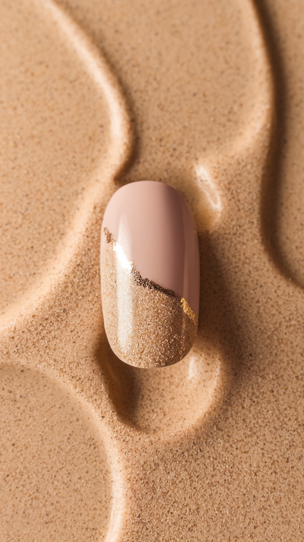 Nail design featuring a nude base with a sandy texture and gold accents, set against a sandy background.